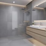 Une salle de bains moderne rénovée, équipée d'une douche à l'italienne, présente un carrelage grand format gris et un meuble suspendu en bois clair, offrant un espace de confort et de bien-être. Cette transformation haut de gamme illustre parfaitement les tendances actuelles en matière de rénovation de salle de bains.