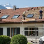 L'image montre des artisans en train de rénover la toiture d'une villa en Suisse. On peut voir des tuiles en cours de remplacement et des travaux d'isolation en cours, illustrant une étape importante d'un projet de rénovation du toit.